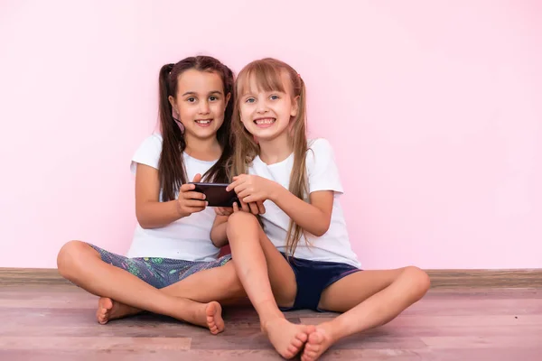 Dos niñas jugando con teléfonos inteligentes sobre un fondo rosa — Foto de Stock