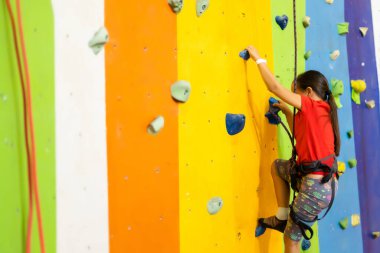 Sportif küçük kız spor salonunda yapay kayaya tırmanıyor.