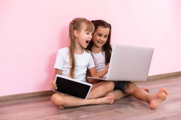 Twee kleine meisjes zitten achter een laptop en lachen, close-up, positieve emoties, entertainment op het internet voor kinderen — Stockfoto