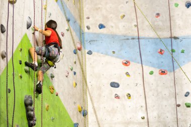 Sportif küçük kız spor salonunda yapay kayaya tırmanıyor.