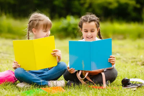 Dos colegialas bonitas se sientan con libros al aire libre en el parque. Colegialas o estudiantes se les enseña lecciones en la naturaleza. — Foto de Stock