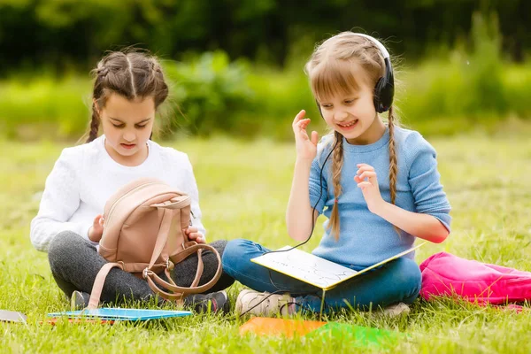 Twee leuke multiculturele schoolmeisjes zitten op het gazon onder de boom en samen lezen boek — Stockfoto