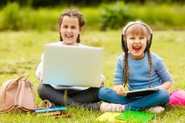 Dvě legrační školačky sedí na trávě a čtou knihy. Dívky, přítelkyně, sestry dostávají lekce v přírodě. — Stock fotografie