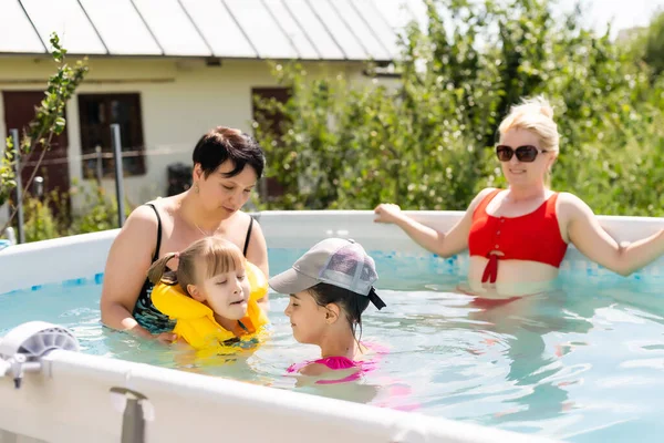 Mère et deux filles jouent dans l'eau de la piscine.Femme et deux filles s'amusent dans la piscine à la maison éclaboussant d'eau et souriant — Photo