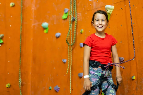 Sporty little girl climbing artificial boulder on practical wall in gym — Stock Photo, Image