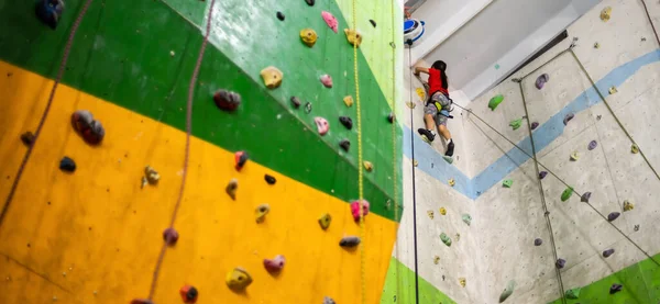 Sportig liten flicka klättring konstgjord sten på praktisk vägg i gym — Stockfoto