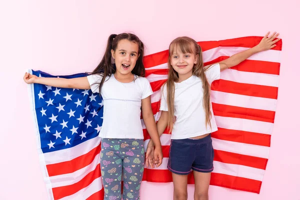 Dos adorables hermanitas sosteniendo banderas americanas sobre un fondo rosa —  Fotos de Stock