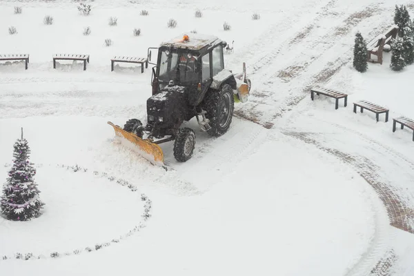 Tractor-excavadora elimina la nieve en el patio de la ciudad. trabajo de los servicios públicos —  Fotos de Stock