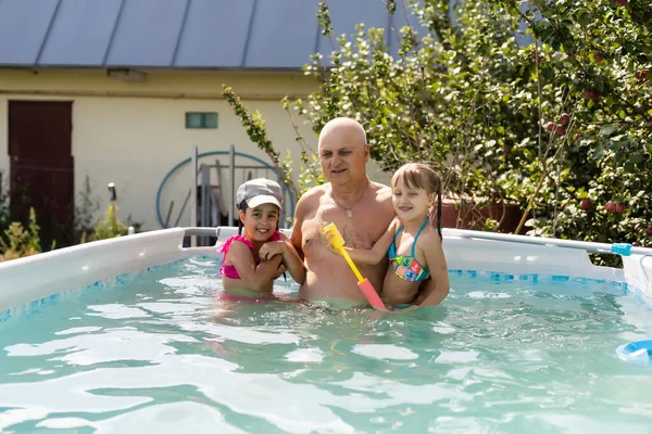 Feliz abuelo activo con nietos divirtiéndose juntos en la piscina —  Fotos de Stock