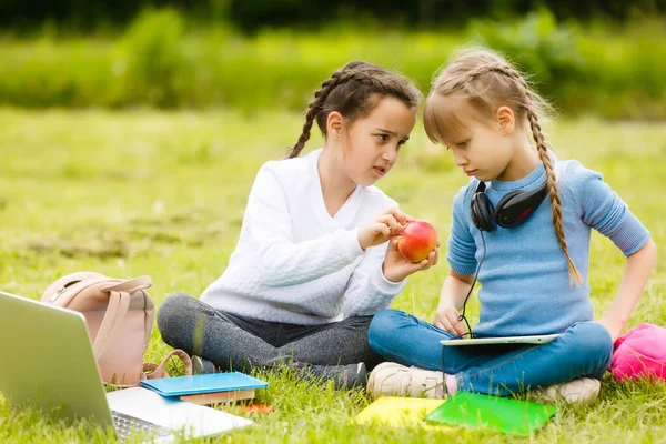Pupils of primary school with lunch-boxes in hands. Girls with backpacks are eating on the lawn. Beginning of lessons. First day of fall. — Stock Photo, Image