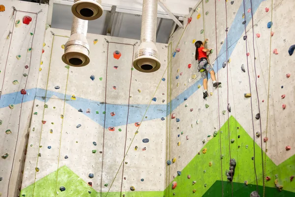 Deportiva niña escalando roca artificial en la pared práctica en el gimnasio — Foto de Stock