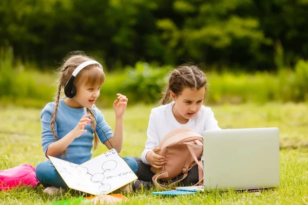 two funny schoolgirls sit on the grass and read books. Girls, girlfriends, sisters are taught lessons in nature.