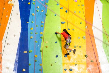 Sportif küçük kız spor salonunda yapay kayaya tırmanıyor.