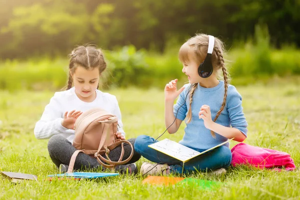 Twee mooie schoolmeisjes zitten met boeken buiten in het park. Schoolmeisjes of studenten krijgen les in de natuur. — Stockfoto