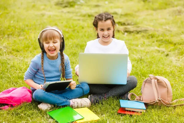 two funny schoolgirls sit on the grass and read books. Girls, girlfriends, sisters are taught lessons in nature.