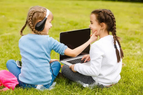 Дві кумедні школярки сидять на траві і читають книги. Дівчата, подружки, сестри навчаються урокам на природі . — стокове фото