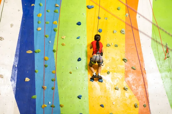 Menina desportiva escalada pedregulho artificial na parede prática no ginásio — Fotografia de Stock