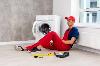 Tulumlu tesisatçı, evdeki çamaşır makinesini tamir ediyor.