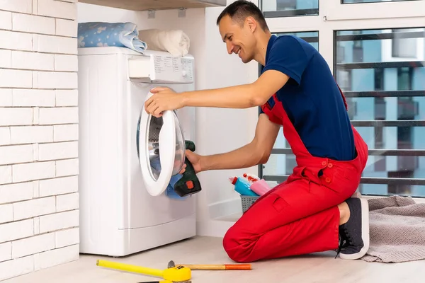 Υδραυλικός σε φόρμες με εργαλεία επισκευάζει ένα πλυντήριο ρούχων στο σπίτι — Φωτογραφία Αρχείου