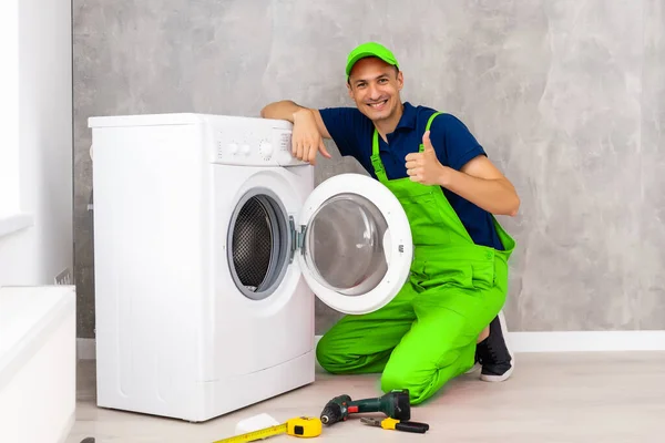 Banyoda çamaşır makinesini kontrol eden aletli yetişkin bir tamirci. — Stok fotoğraf