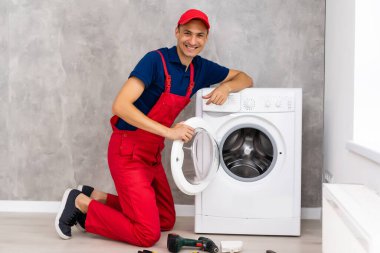 Tulumlu tesisatçı, evdeki çamaşır makinesini tamir ediyor.