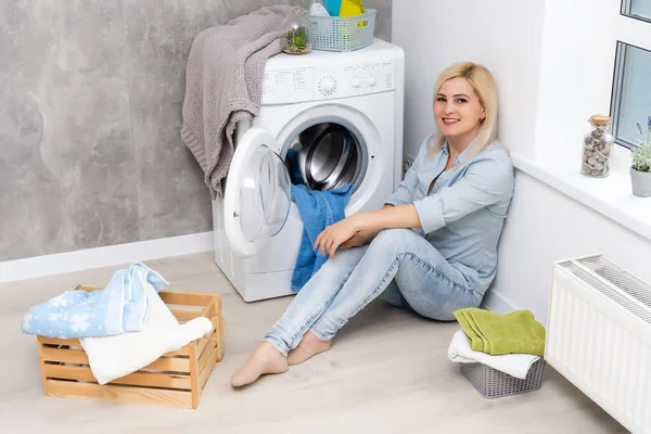 Egy fiatal háziasszony mosógéppel és ruhákkal. Mosás napja. — Stock Fotó