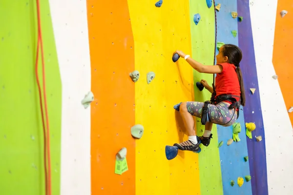 Menina desportiva escalada pedregulho artificial na parede prática no ginásio — Fotografia de Stock