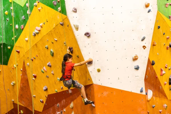 Deportiva niña escalando roca artificial en la pared práctica en el gimnasio —  Fotos de Stock