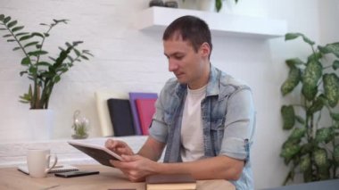 Evdeki masada tabletle çalışan adam.