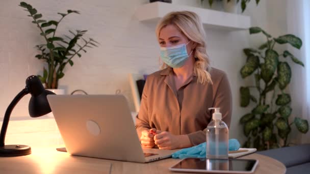 Конец карантина. Молодая женщина работает в офисе за ноутбуком, уставшая от карантинных мер, раздраженная, снимает медицинскую маску — стоковое видео