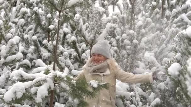 白い服を着た女の子が雪の中の松の木の近くに立っている. — ストック動画