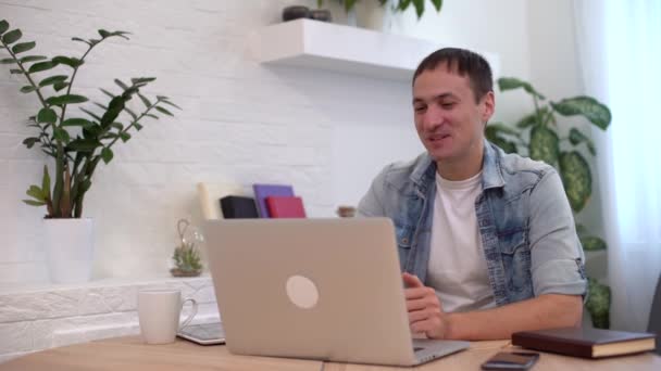 Технології, віддалена робота і концепція способу життя щасливий чоловік з ноутбуком, який має відеочат і махає рукою в домашньому офісі — стокове відео