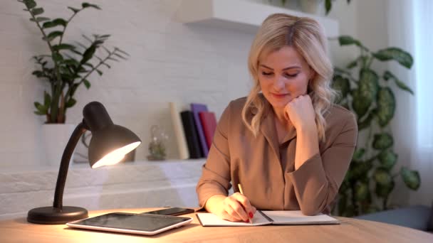 Donna caucasica positiva che prende penna e scrive un piano aziendale. Ritratto di giovane sarto felice seduto in atelier con macchina da cucire sul tavolo. Piccola imprenditorialità. — Video Stock