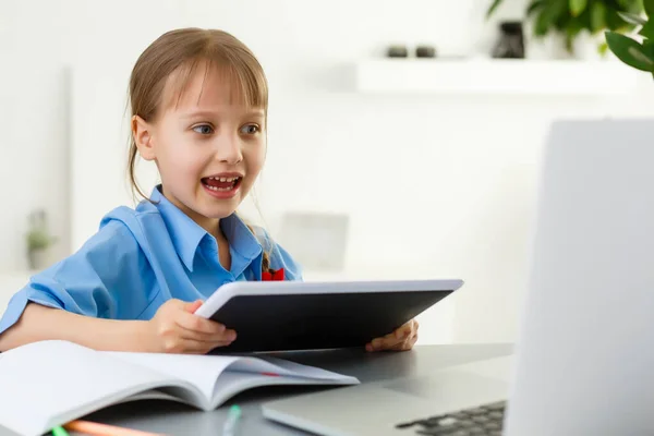 Linda niña está sentada en la mesa con su computadora portátil y estudiar en línea —  Fotos de Stock