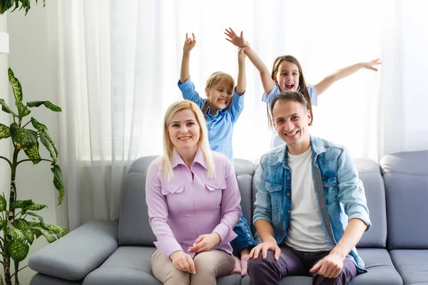 Joyeux jeune famille avec des enfants riant assis sur le canapé ensemble, les parents avec des enfants appréciant divertir à la maison — Photo