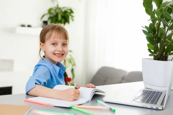 Söt liten flicka sitter vid bordet med sin bärbara dator och studerar online — Stockfoto