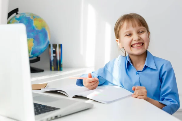 Schattig klein meisje zit aan tafel met haar laptop en studeren online — Stockfoto