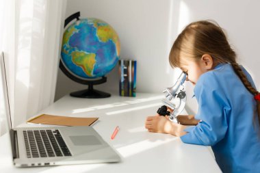 Uzaktan eğitim. Çocuk mutlu bir şekilde gülümser ve uzaktan bilgi alır. Küçük kız evden online öğrenim görüyor. Çevrimiçi okul.