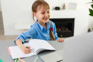 Şirin küçük kız laptopuyla masada oturuyor ve internetten ders çalışıyor.