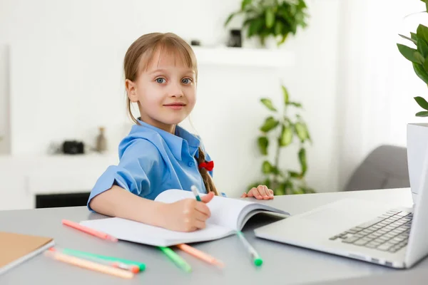 Menina bonito está sentado à mesa com seu laptop e estudando on-line — Fotografia de Stock