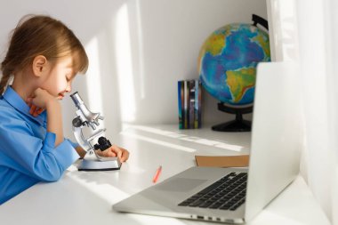 Uzaktan eğitim. Çocuk mutlu bir şekilde gülümser ve uzaktan bilgi alır. Küçük kız evden online öğrenim görüyor. Çevrimiçi okul.