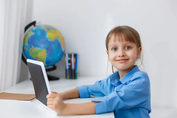 Roztomilá holčička sedí u stolu se svým notebookem a studuje online — Stock fotografie
