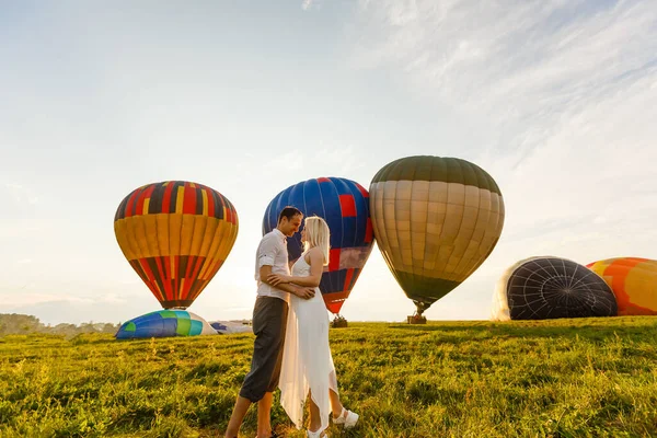 Mooi romantisch koppel knuffelend op weide. hete lucht ballon op een achtergrond — Stockfoto