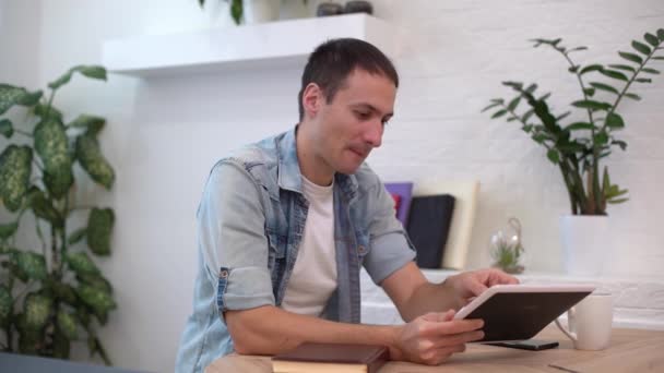Man die thuis met tablet aan tafel werkt — Stockvideo