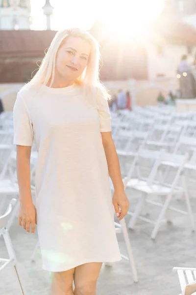 Vonzó nő öltözött fehér ruha nyáron szabadtéri színház széken egyedül, tavaszi utcai divat trend, társadalmi távolság — Stock Fotó