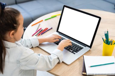 Akıllı küçük beyaz kız laptopun başına oturur not defterine not alır, küçük kız el yazısı evde ödev hazırlar, uzaktan eğitim kavramı oluşturur.