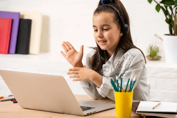 A menina feliz em fones de ouvido com um laptop sentado à mesa — Fotografia de Stock