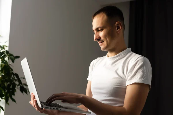 Travailler avec joie. Beau jeune homme utilisant son ordinateur portable et sourire tout en se tenant debout sur fond blanc. — Photo