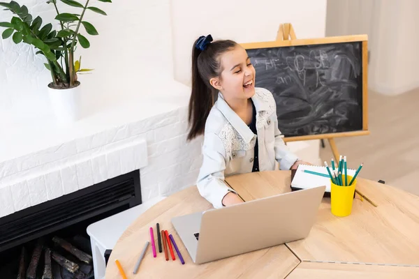 Pequeña niña caucásica inteligente niño sentarse en el estudio de la mesa en el ordenador portátil hacer notas escribir en el cuaderno, pequeña colegiala escritura a mano preparar tarea asignación en casa, concepto de educación a distancia — Foto de Stock