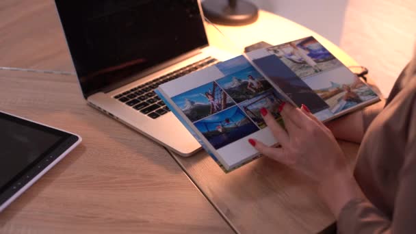 Женщина держит и представляет фотокнигу рядом с ноутбуком — стоковое видео